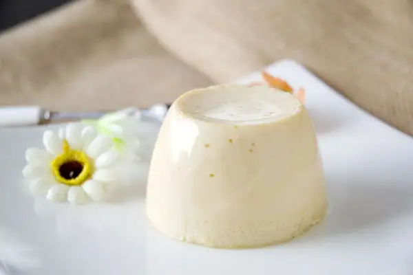 Budino fatto in casa, liscio e cremoso, servito su un piatto bianco con un fiore decorativo.