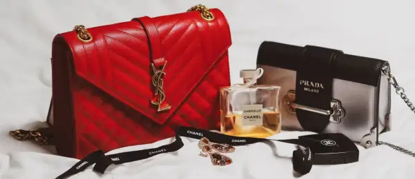 En röd, quiltad modalu väska med gulddetaljer, bredvid en Prada-väska, Chanel-parfym och smycken.