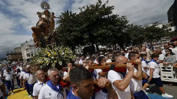 Procesión de la Virgen en las fiestas del Carmen de Foz. Hombres portan la imagen adornada con flores, mientras una multitud observa.