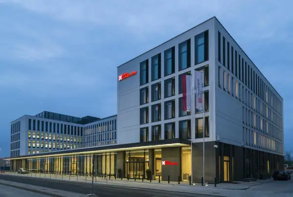 Nowoczesny budynek Hilton Garden Inn Kraków o białej fasadzie z czerwonym logo, z polską flagą przy wejściu.