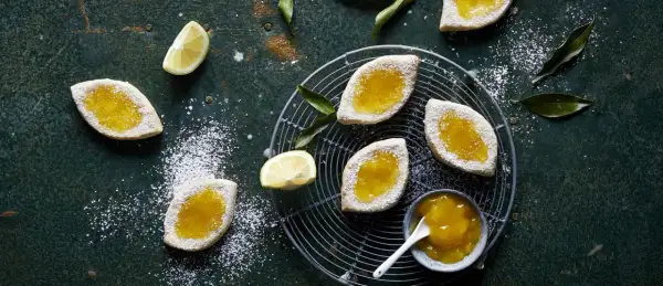 Italienische Kekse mit Lemon Curd, bestäubt mit Puderzucker, auf einem Gitter und dunklem Untergrund.