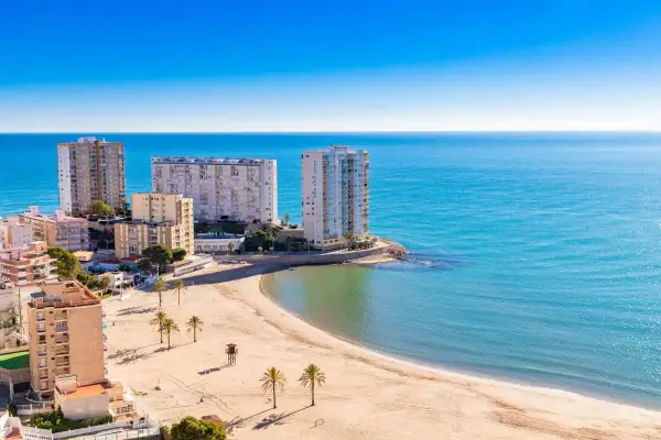 Edificios altos y una playa dorada en el balneario Cullera, con el mar azul brillante de fondo.
