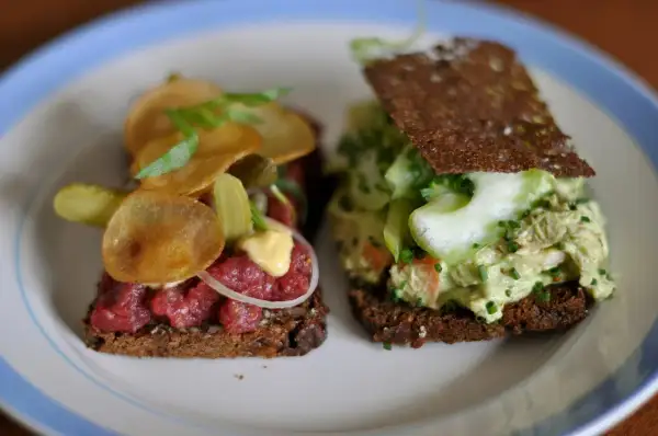 Dos sándwiches abiertos, uno con tartar de ternera y patatas fritas, otro con ensalada de pollo y pepino. Comida típica de Dinamarca.