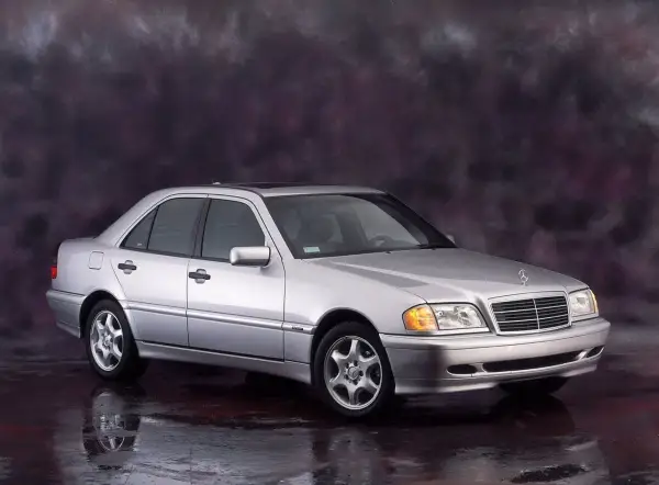 Srebrny Mercedes-Benz C-Klasa W202 z lat 90. na tle ciemnego, malowanego tła.