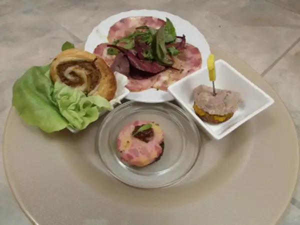 Verschiedene Tapas mit Fleisch: ein Fleischröllchen im Blätterteig, ein kleiner Burger mit Fleisch und ein Stück Fleischpastete.