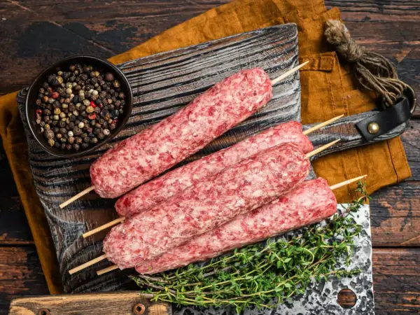 Surowe kofty wołowe na patyczkach, gotowe do grillowania, obok miseczki z pieprzem i gałązki tymianku.