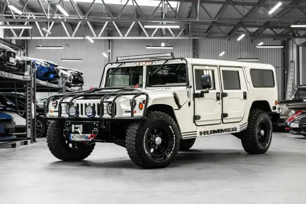 Biały Hummer H1 z potężnymi oponami i dodatkowym oświetleniem na dachu, gotowy na każdą przygodę.
