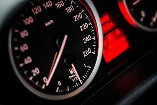 Velocímetro de coche con aguja marcando 120 km/h. El indicador de combustible marca casi lleno. Las luces de advertencia rojas brillan.