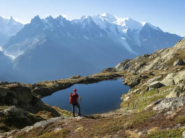 Widok na wejście na Mont Blanc. Turysta z plecakiem stoi nad górskim jeziorem, podziwiając ośnieżone szczyty.