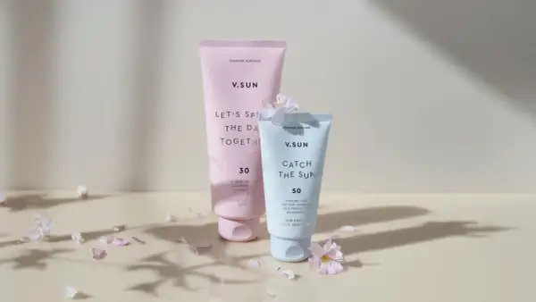 Zwei V.SUN Sonnencreme-Tuben, eine mit LSF 30 für den Körper, die andere mit LSF 50 für das Gesicht, umgeben von zarten Blütenblättern.