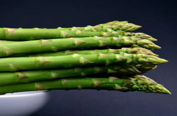 A stack of fresh green asparagus spears with water droplets, against a dark background.
