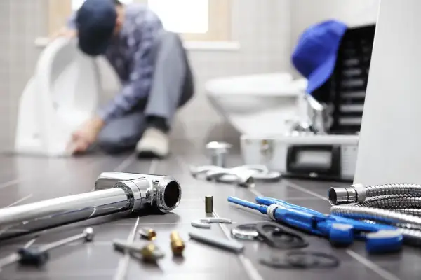Idraulico al lavoro su un water, con attrezzi e tubi in primo piano. La pendenza scarico cucina è fondamentale per un corretto deflusso.