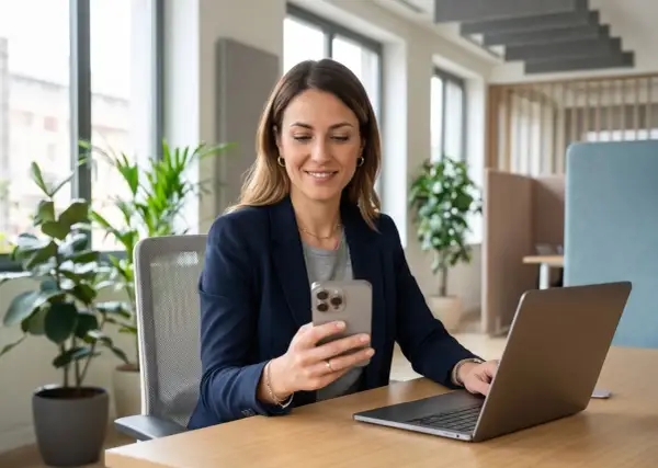 Donna sorridente al telefono, con un laptop aperto. Sembra che stia organizzando la sua astensione dal lavoro.