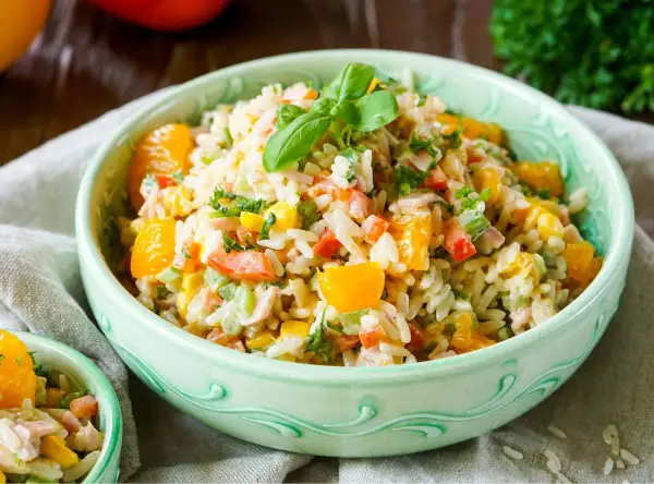 Ein erfrischender reis salat mit Orangenstücken, Paprika, Mais und Kräutern, garniert mit Basilikum.