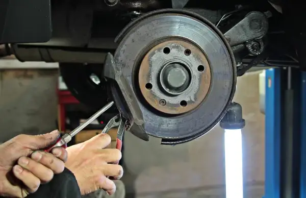 Mains d'un mécanicien utilisant des outils pour changer un disque de frein usé sur une voiture.