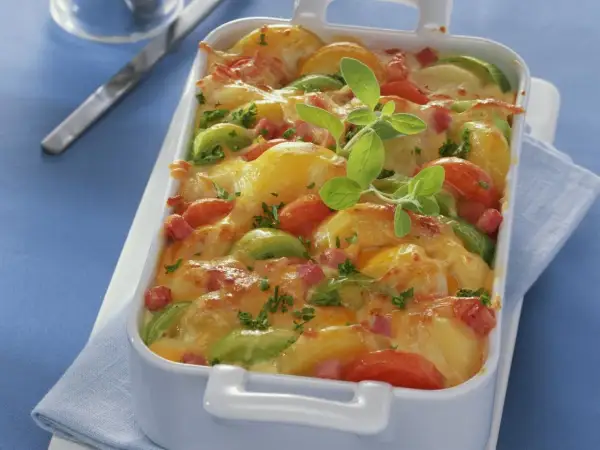Herzhaftes Kartoffel Lauch Gratin mit Tomaten und Speck, überbacken mit goldbraunem Käse und garniert mit frischen Kräutern.