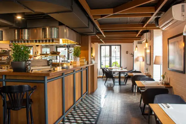 Wnętrze restauracji Magiel: drewniany bar, czarne krzesła, stoliki z białymi obrusami i nowoczesne oświetlenie tworzą przytulną atmosferę.