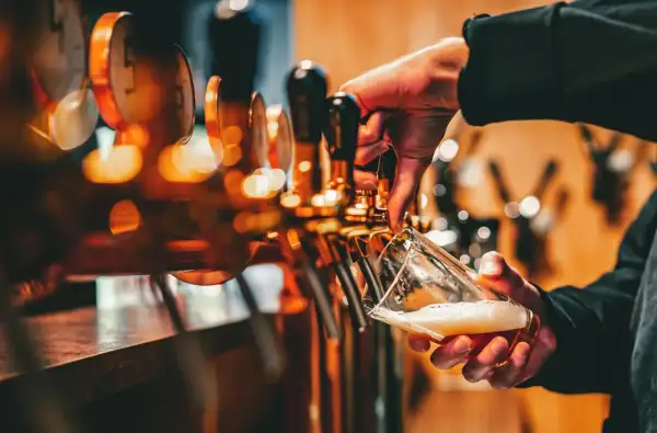 Mano che versa birra da una spillatrice, creando una schiuma perfetta. La spillatura alla tedesca è un'arte.