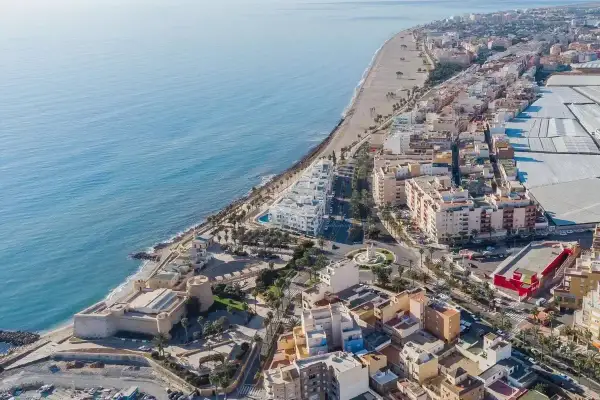 Vista aérea de la costa de Almería, Roquetas de Mar, con el mar azul, la playa, edificios residenciales y un castillo histórico.
