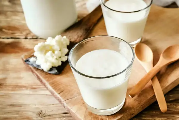 Två glas med krämig kefir står på en träskärbräda. Bredvid syns kefir-kultur och två träskedar. Kefir nyttigt för magen!