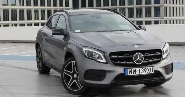 Szary Mercedes GLA 220 z polskimi tablicami rejestracyjnymi stoi na parkingu przed nowoczesnym budynkiem.