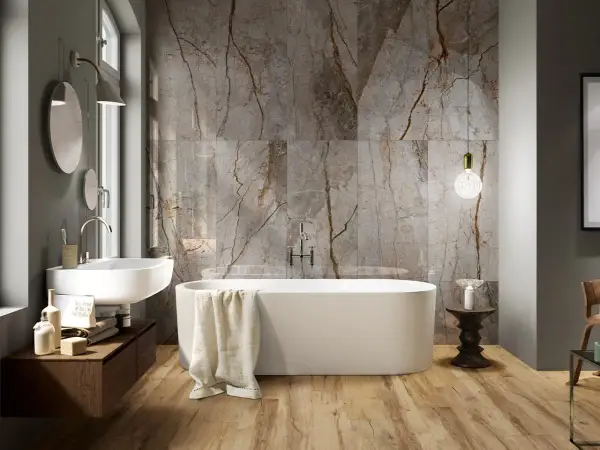 Bagno moderno con vasca freestanding, lavabo sospeso e parete in marmo con venature che si abbinano al legno del pavimento. Idee bagno marmo e legno per un ambiente di lusso.