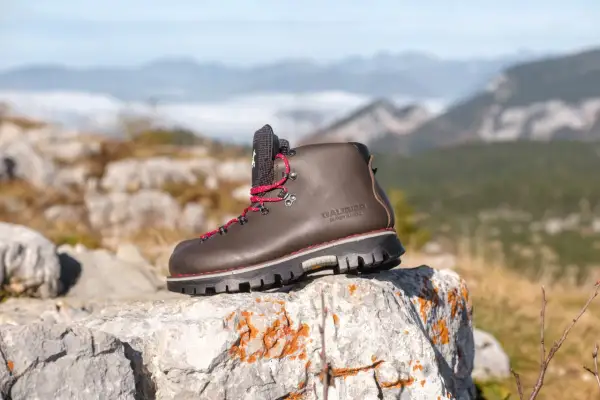 Une bonne chaussure de marche marron, lacets rouges, sur un rocher, avec des montagnes brumeuses en arrière-plan.