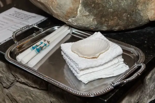 Sur un plateau argenté, des bougies ornées de colombes et d'une croix bleue, symboles de la démarche baptême, attendent près d'une coquille et de serviettes blanches.