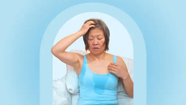 A woman experiencing night sweats after working out, with sweat visible on her tank top and forehead.
