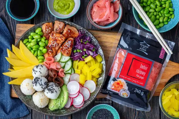 Kolorowy bowl z kawałkami łososia, edamame, mango, awokado, ryżowymi kulkami i marynowanym imbirem. Obok opakowanie różowego imbiru.
