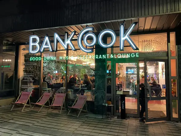 Nietypowe restauracje Poznań: neonowy szyld "BANKOOK" nad wejściem do lokalu z ogródkiem i stolikami w środku.