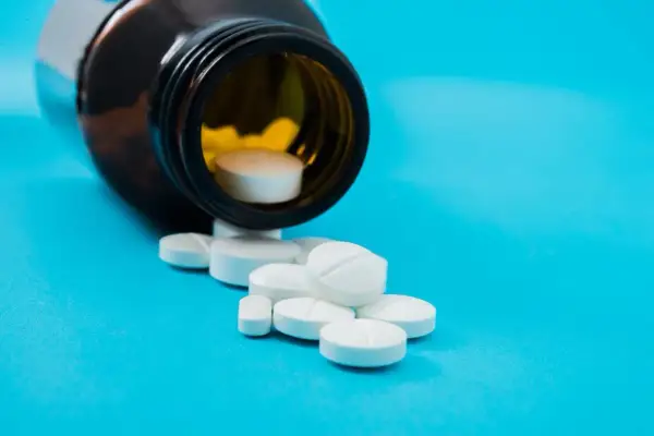 Białe tabletki, w tym jedna z nacięciem, wysypują się z brązowej butelki. To może być vicodin.