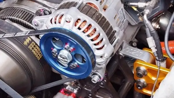 Detalle de un alternador de coche, listo para cambiar. Se aprecian la polea azul y la correa.