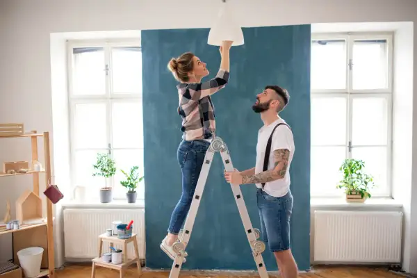 Coppia installa un lampadario, una delle migliorie che aumentano il valore di un immobile.