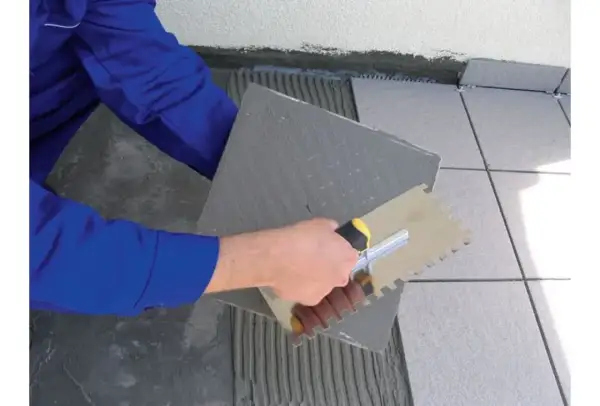 Układanie płytek na tarasie, tworząc płynne połączenie tarasu z domem. Ręka z kielnią rozprowadza klej.