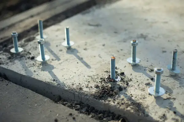 Kilka metalowych kotew z podkładkami i nakrętkami osadzonych w betonie.
