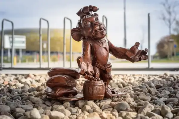 Figurka krasnala z beczką i workami, jeden z lwy gdańskie, stoi na kamieniach przed stadionem.