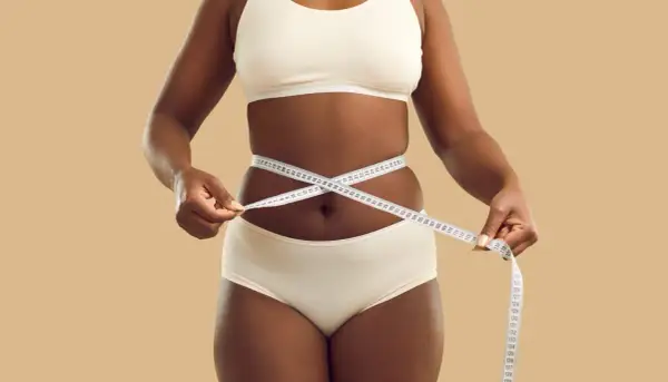 Une femme mesure sa taille avec un mètre ruban, symbolisant son objectif de perdre 5 kilos en 1 mois.