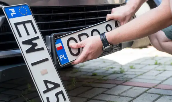 Ręce montują polską tablicę rejestracyjną. Nowe oznaczenie pojazdu gotowe do drogi.