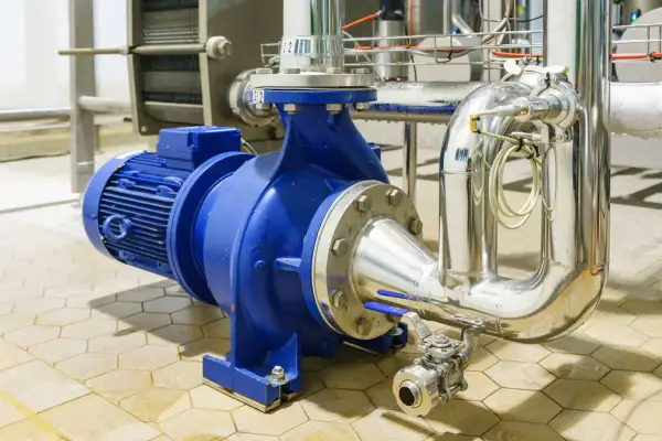 Pompe industrielle bleue connectée à des tuyaux en acier inoxydable. L'ensemble est conçu pour gérer des fluides sous haute pression.