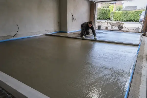 Pracownik wyrównuje świeżą wylewkę betonową, używając poziomicy. To kluczowy etap, jak zrobić prowadnice do wylewki, by uzyskać idealnie gładką powierzchnię.