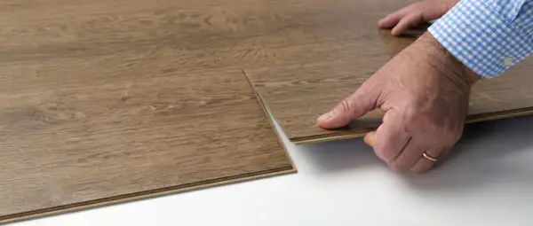 Close-up of a hand performing vinyl floor installation, clicking two wood-look planks together.