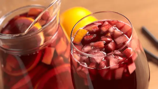 Un bicchiere e una caraffa pieni di vino per sangria, con pezzi di frutta e fette d'arancia.