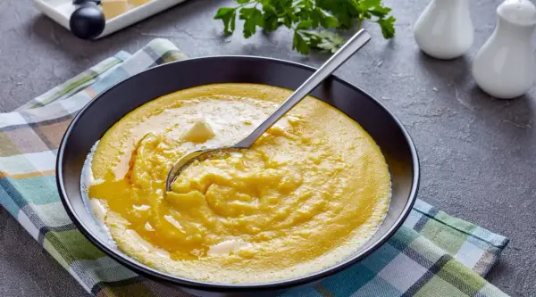 Cremige Polenta mit Butter in einer schwarzen Schüssel, bereit für ein köstliches polenta rezept. Ein Löffel ruht darin.