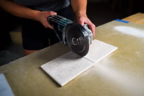 Hands carefully cutting decorative porcelain tile with an angle grinder, creating a clean line.