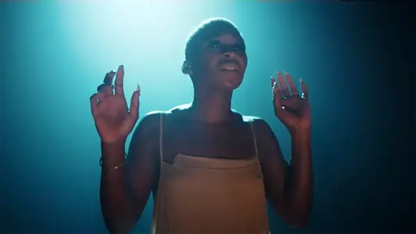 Cynthia Erivo stand up, wznosi ręce w górę, w świetle reflektorów.
