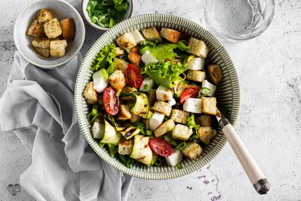 Deliziosa insalata di zucchine grigliate, pomodorini, cubetti di formaggio fresco e crostini croccanti, guarnita con erba cipollina.