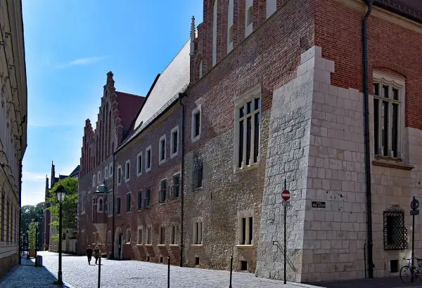 Kamienne i ceglane mury Collegium Maius w Krakowie, z charakterystycznymi oknami i detalami architektonicznymi, na tle błękitnego nieba.