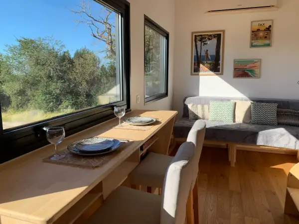 Intérieur d'une tiny house dans les Landes, avec un coin repas face à la nature et un canapé confortable.