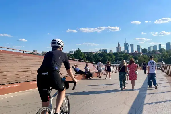 Rowerzysta na trasie rowerowej wzdłuż Wisły w Warszawie, z widokiem na panoramę miasta.